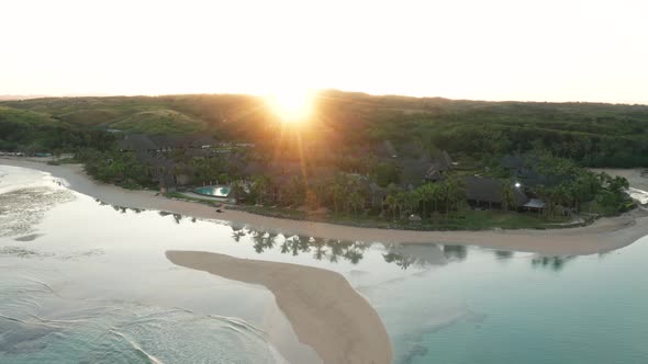 Bright sun shines over hill into tropical bay on shore of mainland Fiji, aerial