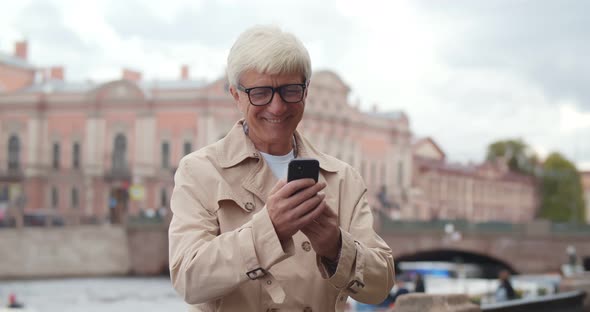 Smiling Middle Age Businessman Using Smartphone Standing Near City River