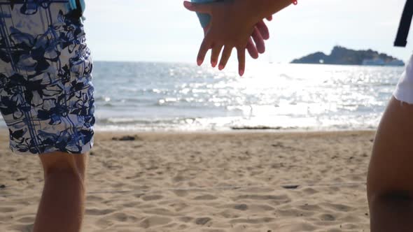 Young Couple Taking Hands of Each Other and Running Along Beach To Sea