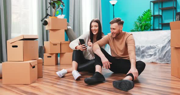 Young Couple are Using Phone Amid Boxes in a New House