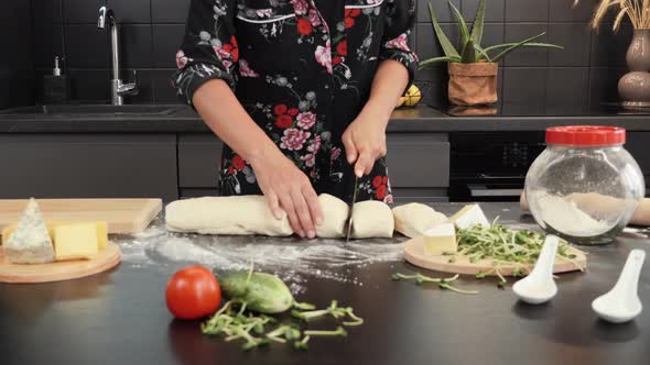 Female hands cutting raw dough into small pieces.