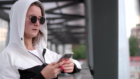 Stylish Young Girl Uses a Smartphone She is Wearing Sunglasses