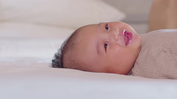 An Asian newborn baby is laying down on a soft white sheet mattress. Starring at his parents and fee