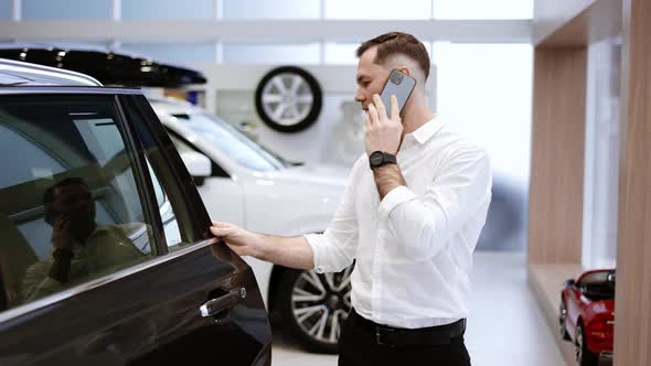 Young Man Using Phone While Chooses a New Model of a Luxury Car in Showroom