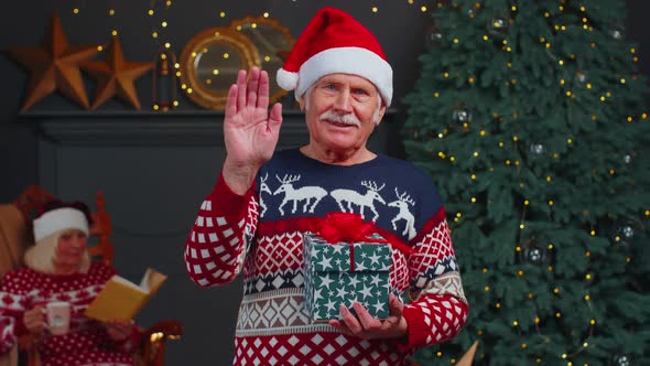 Senior Grandfather in Christmas Sweater Smiling Friendly at Camera and Waving Hands Gesturing Hello