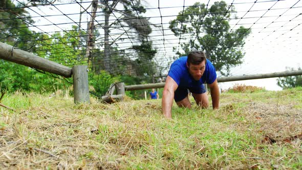 Fit man crawling under the net during obstacle course 4k