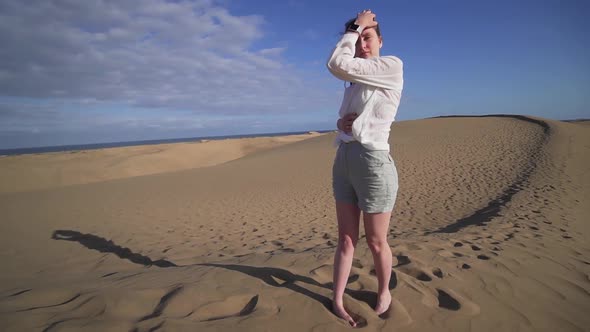 A Beautiful Female Model in a Desert Journey Stands on a Dune Ridge at Sunset and Poses, Fashion