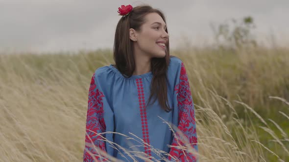 Attractive Young Brunette Girl with Red Flower in Hair and Beautiful Blue Long Summer Dress Standing