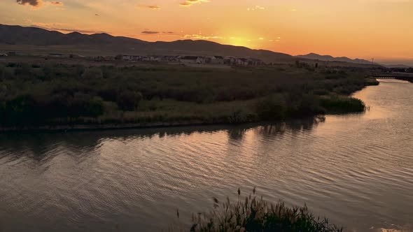 Moving time lapse or hyperlapse of a sunset beyond a river in a rural setting with mountains and foo