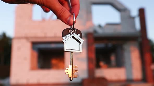 Hand with the key to the future house on the background of a construction site and walls