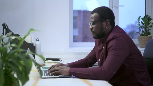 African Businessman Behind Laptop Works in Office Against Background of Window Spbas