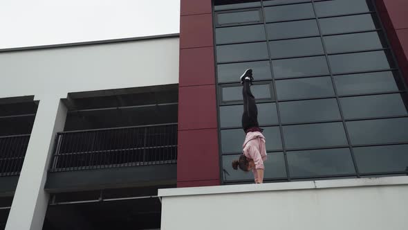 Young Female Gymnast Performs Handstand, on Area Near Modern Buildings.