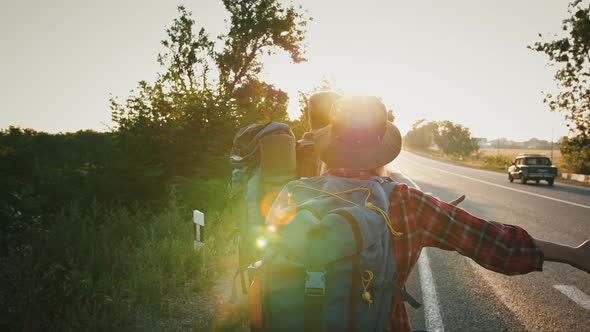 Tracking Shot of Couple of Tourists Hitchhiking on Highway in Evening