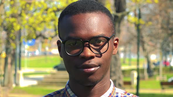 A Young Black Man Puts on Glasses and Smiles at the Camera in a Park on a Sunny Day - Face Closeup