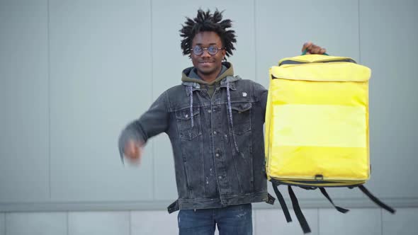 Cheerful African American Young Man Showing Thumb Up Raising Yellow Insulated Food Delivery Bag