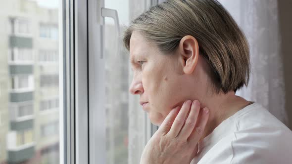 Woman Looks Out of Window and Touches Painful Spot on Neck