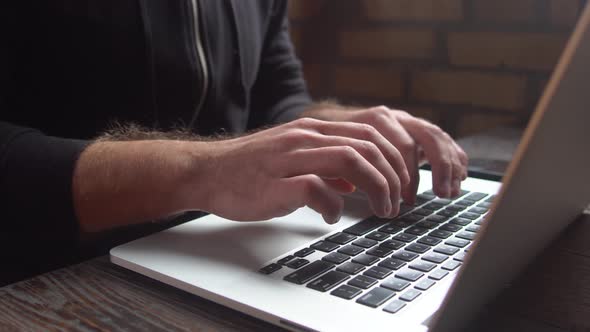 Man typing on laptop keyboard in the loft cafe. Close up man hands writing on laptop keyboard.