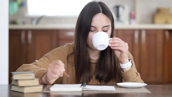 Young Beautiful Girl Makes Entries in Her Diary While Sitting at a Table