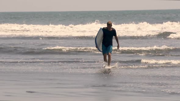 Guy walking out of the surf after having an amazing session on the waves.