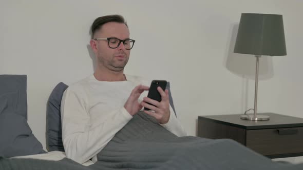 Casual Man Using Smartphone in Bed