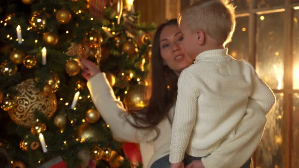 Young Mother in a White Blouse Decorates a Christmas Tree with Her Son