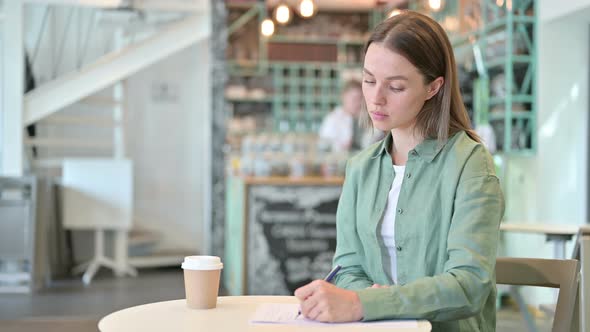 Woman Thinking and Writing on Paper in Cafe 