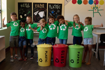 Group of schoolchildren holding color coded recycling bins and bags  in an elementary school classro