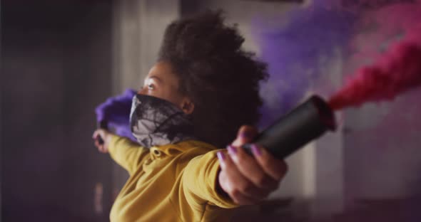 Mixed race woman holding blue and purple flares standing in an empty building