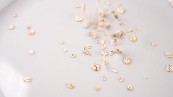 Dry oatmeal falls on a white surface of a plate 