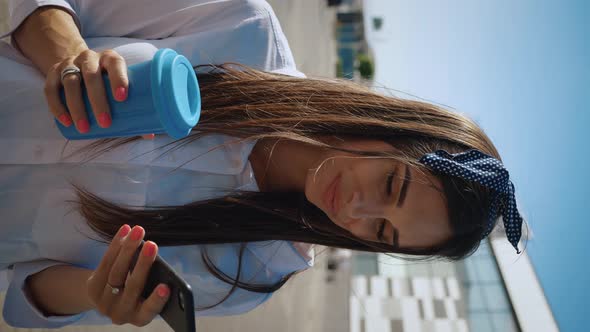 Vertical Video of Young Woman Using Smartphone and Drinking Coffee on Background of Office Building