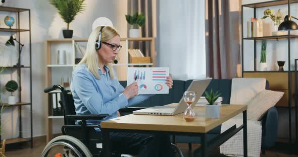Woman in Headphones Sitting in Wheeelchair and Holding Online Meeting with Coworkers