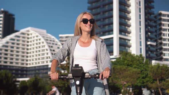 Young beautiful girl rides electric scooter in summer along street,