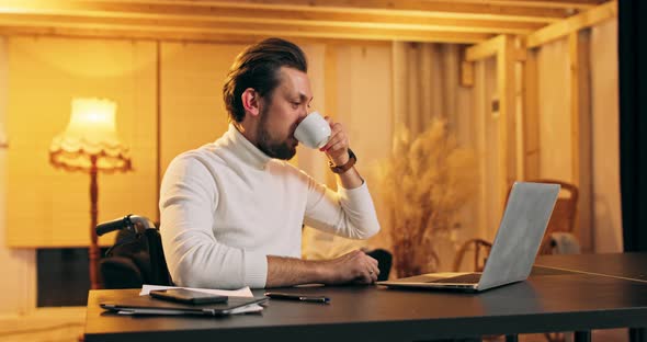 Disabled Man Having Coffee While Using Laptop at Home Young Male Professional Using Computer Sitting