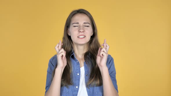 Worried Pretty Woman Standing with Finger Crossed for Good Luck on Yellow Background