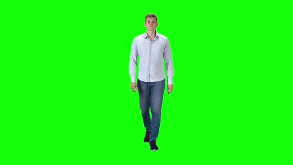 Young Man in a Gray Shirt, Jeans and Sneakers Going Against a Green Background. Slow Motion.