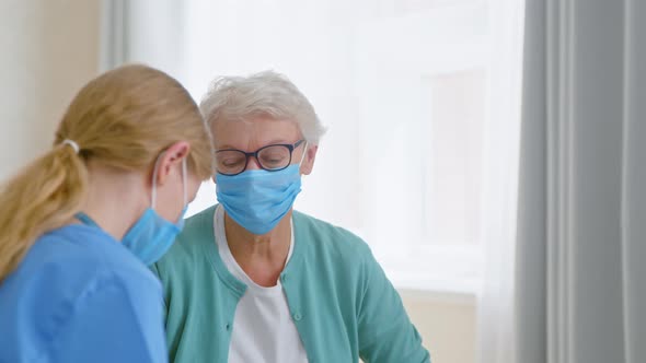 Mature grey haired woman wearing protective mask talks to nurse