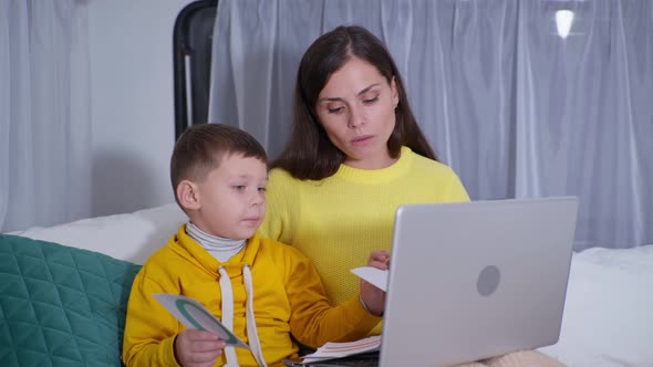 Female Parent with Her Son Takes Online Lessons with Teacher Via Video Link on Laptop While
