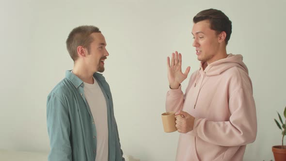 Young Lgbt Men are Talking to Each Other Standing in the Center of the Living Room and Laughing