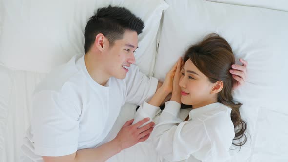 Portrait of Asian new marriage couple lying on bed and look each other.