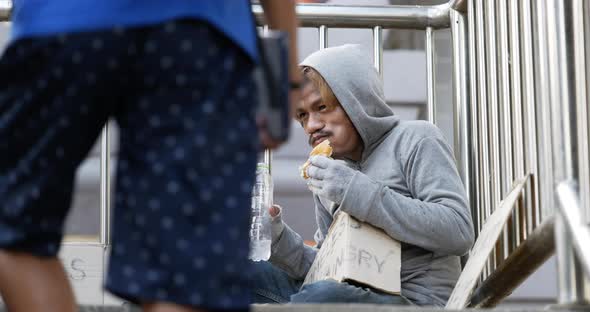 Homeless man drinking water and eating food on the overpass