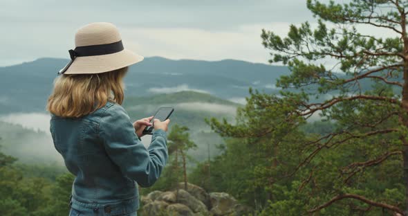 A Woman is Standing on Top of a Cliff and Texting a Message on Her Smartphone