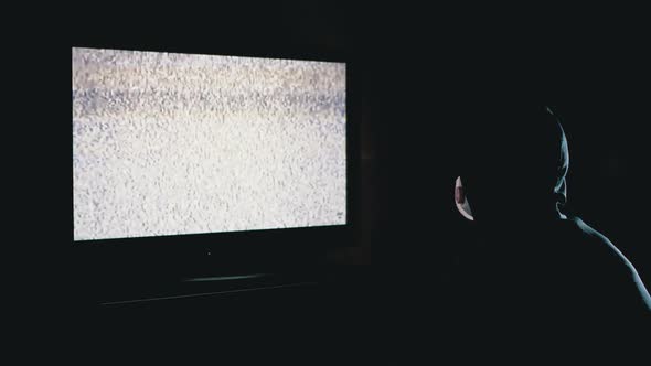 Silhouette of Man in Hood and Medical Mask Watching TV with Static Interference