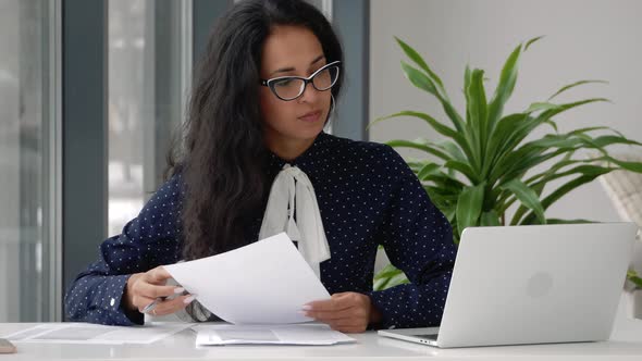 Female entrepreneur reading documents, analyzing financial papers, preparing audit report at workpla