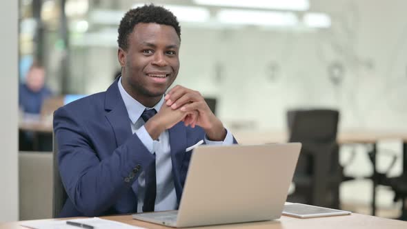 African Businessman Smiling at Camera While Working on Laptop