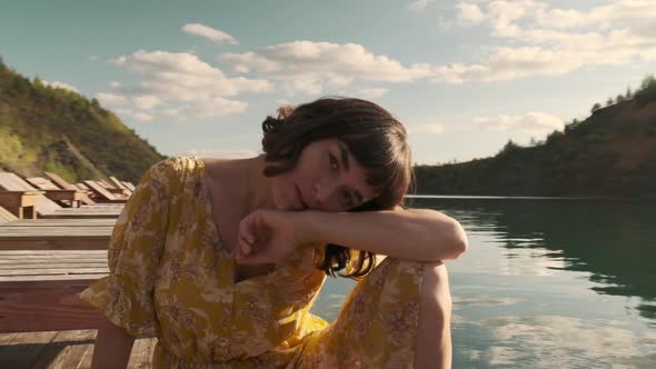 A young girl in a yellow dress sits on a wooden pier