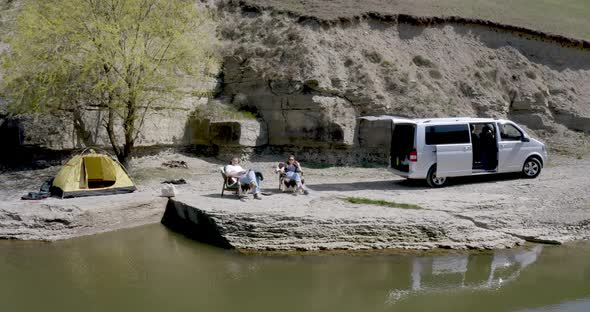 drone view of a guy and a girl sitting on armchairs in a campsite on the lake near the motor home