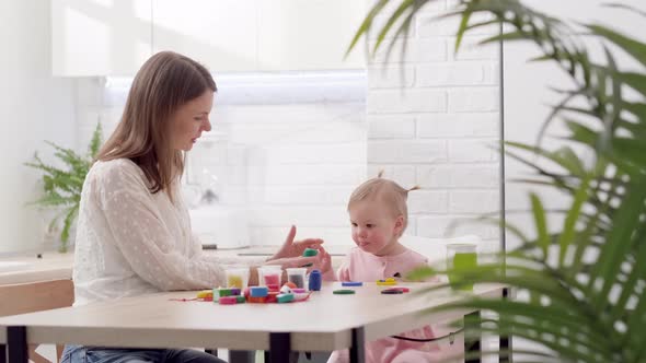 Mom and Little Daughter Sitting in Kitchen and Playing Multicolored Plasticine Mother and Daughter