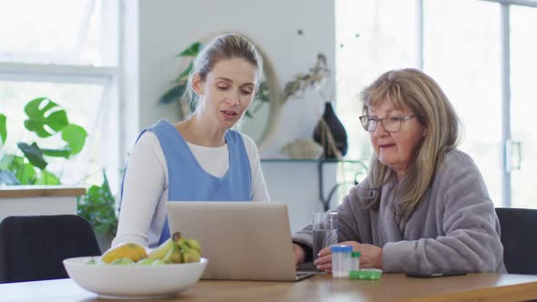 Female health worker and senior woman discussing over laptop at home