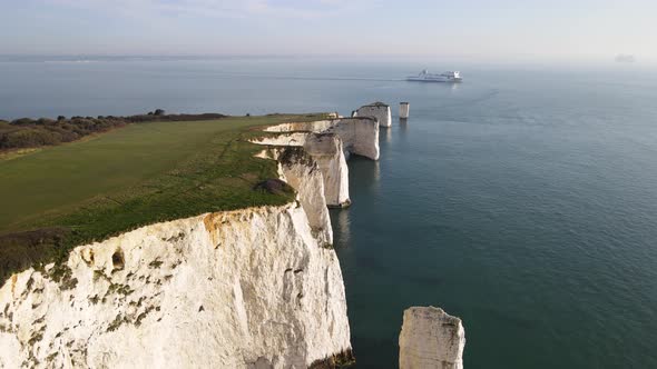 Aerial forward over white and jagged cliffs of Old Harry Rocks and ship cruising in background, Purb