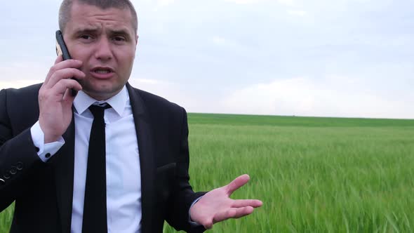 Angry Businessman Talking on a Smartphone in the Middle of the Field